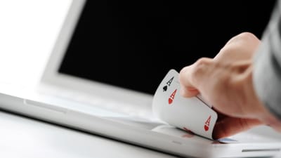 En hand med två ess vilar på en vit, bärbar, dator.