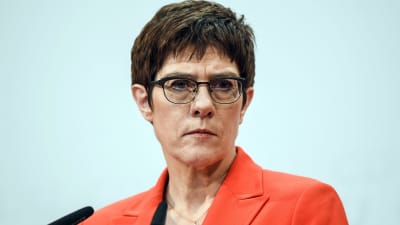 Annegret Kramp-Karrenbauer med sammanbiten min framför en mikrofon under en presskonferens. Hon har en röd kavaj på sig och glasögon med svarta bågar.