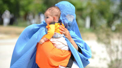 En afghansk kvinna iklädd blå burka bär på ett litet barn. Hon återvänder frivilligt från Pakistan till hemlandet.