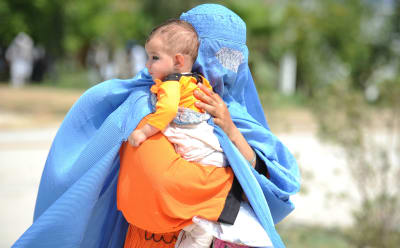 En afghansk kvinna iklädd blå burka bär på ett litet barn. Hon återvänder frivilligt från Pakistan till hemlandet.