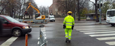 En arbetare i gula arbetskläder går över gatan vid övergångsstället vid Åbo Domkyrka, och en bil åker förbi utan att stanna för honom.