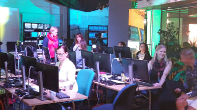 Människor sitter vid datorer i kulisserna till Yles OS-studio.
