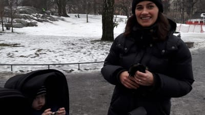 Veronica Stenius, småler mot kameran, med ett barn som tittar fram ur vagnen.
