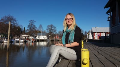 En kvinna sitter på en kajkant i Ingå, hon heter Saara Rapeli.