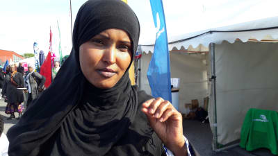Fadumo said i svart niqab, med ena handen höjd, som i ett samtal. Partitält i bakgrunden. 