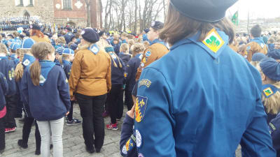 Scouter i olika färgers scoutriggar och baskrar står utanför Åbo Domkyrka inför scoutparaden.