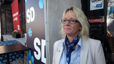 Carina Herrstedt i profil framför SD-logga på husfasad. 