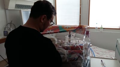 En pappa sköter sin för tidigt födda baby som ligger i en kuvös.