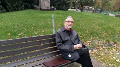 äldre man sitter på parkbank 