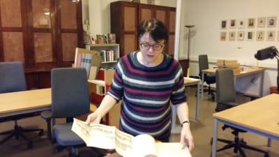 kvinna med kort mörkt hår och glasögon bläddrar i gammal bok