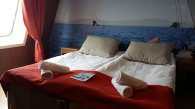 Fartygshytt med rostbrunt täcke och ett foto med en segelbåt på väggen på m/s Finnswan.