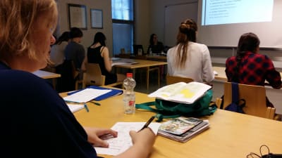 Studerande sitter i ett klassrum och svarar på skriftliga frågor.