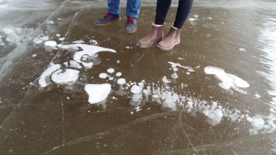Två par skor står vid bubblor som frusit fast i isen.