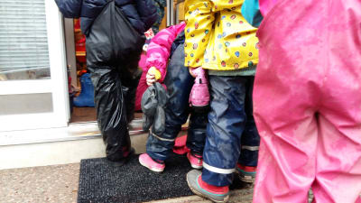 Daghemsbarn i regnkläder köar för att komma in till dagiset.