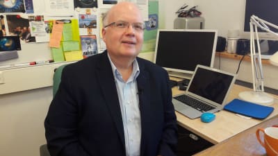 Professor Peter Lund på Aalto-universitetet sitter i ett kontor och tittar in i kameran. 