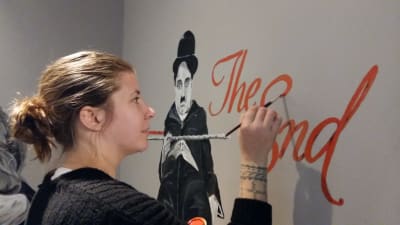 Johanna Karvonen målar Charlie Chaplin och The End på väggen i foajén på en biograf.