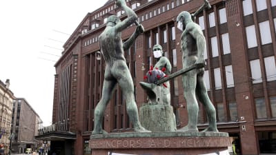 Tre smeder-statyn bär andningsskydd. ''Hålls säker'' står det på statyns fot, och i mitten av statyn finns en boll som liknar coronaviruset.