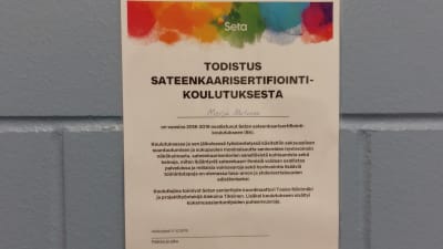 Ett certifkat med regnbågsfärger längst upp, upphängt på väggen i Kampens servicecentral.  