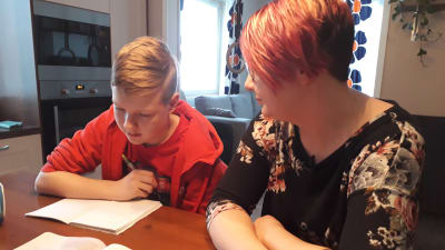Tonårig son med matematikbok och sin mamma