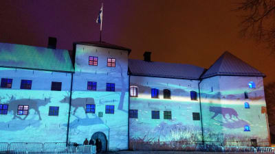 Renar, en björn och Finlands natur projiceras på Åbo slotts fasad i vinternatten i ljusinstallationen Luminous Finland 100.