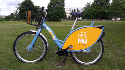 En blågul eFölläri-cykel står på en gräsmatta.