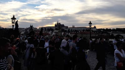 Karlsbron i Prag i skymingen. Massor med människor, i bakgrunden slott