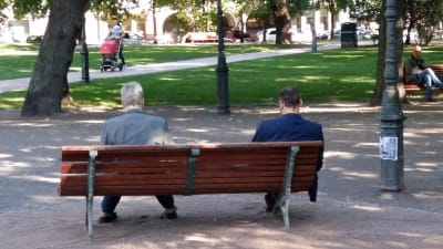 Två män sitter på en parkbänk i Helsingfors.