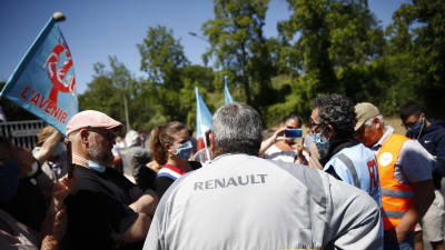 Personer står med ryggen mot kameran. De står utanför en Renaultfabrik i Frankike. På en persons jacka står det Renault.
