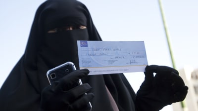 En kvinna i niqab håller upp en böteslapp som hon fått på grund av sitt klädesplagg i Frankrike.