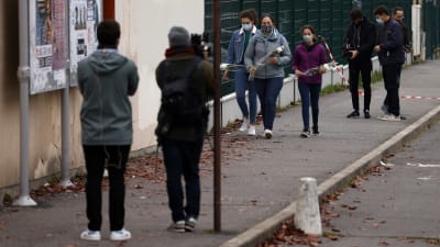 Unga men munskydd hämtar med sig blommor till en skola i Conflans-Sainte-Honorine där en lärare har mördats.