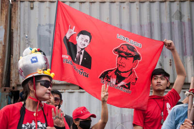 Thailändska demonstranter klädda i röda skjortor håller upp en röd banderoll med en bild av den avsatte ex-premiärministern Thaksin Shinawatra.  