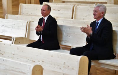 Vladimir Putin och Gennadij Timtjenko sitter på en bänk och applåderar.