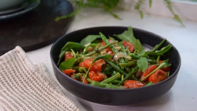 Ett fat med en grön bönsallad med körsbärstomater.