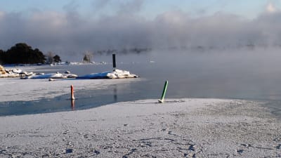 Isen lägger sig utanför Kitö bro i Sibbo skärgård, Kalvön i Borgå skärgård skymtar bakom sjöröken