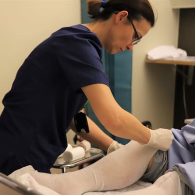 Sairaanhoitaja Edita Mullo laittaa potilaalle tukisukkaa jalkaan.
