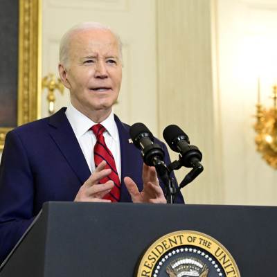 Joe Biden står vid ett talarpodium med presidentens sigill och ser rätt glad ut. Han gestikulerar med händerna.