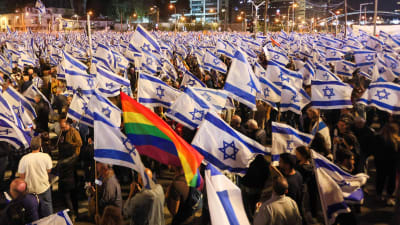 Ett hav av israeliska flaggor med en regnbågsflagga i mitten.