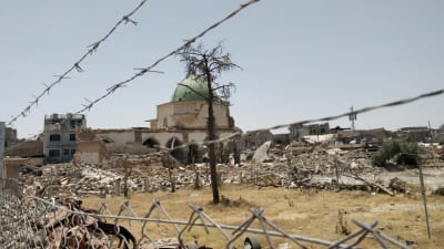 Den numer förstörda Al-Nouri moskén i Mosul skymtar i bakgrunden. I förgrunden stängsel, taggtråd och bråte.