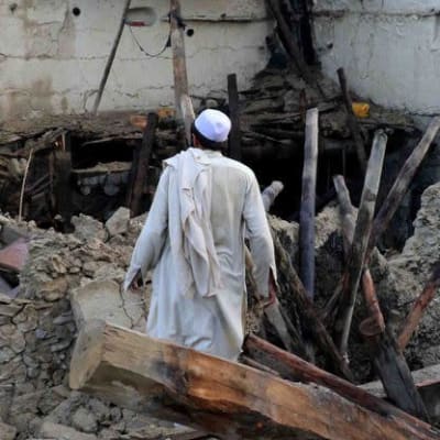 Mies seisoo maanjäristyksessä romahtaneen talon raunioissa.