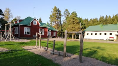 En röd träbyggnad och en ljust stenhus som är Västankvarns skola i Ingå.