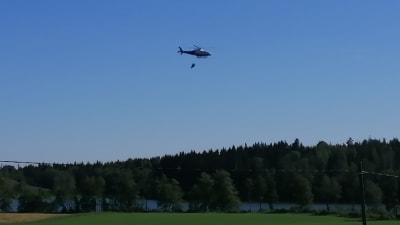 En helikopter flyger med vatten över skogen. 
