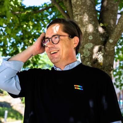 Helsinki Pride -yhteisön puheenjohtaja Panu Mäenpää hymyilee puun varjossa.