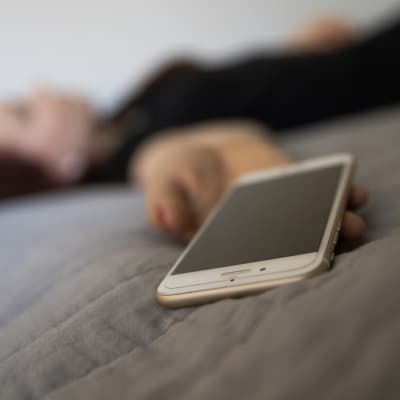 Nainen makaa sängyllä puhelin kädessään.