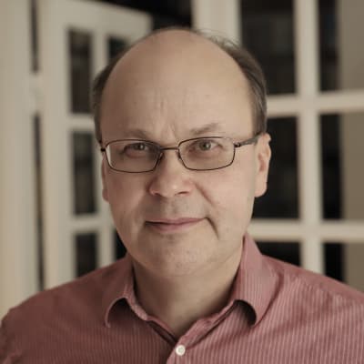 En man i röd skorta står i ett vitt rum. 