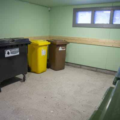 Behållare för olika material som ska återvinnas, finns i ett rum.