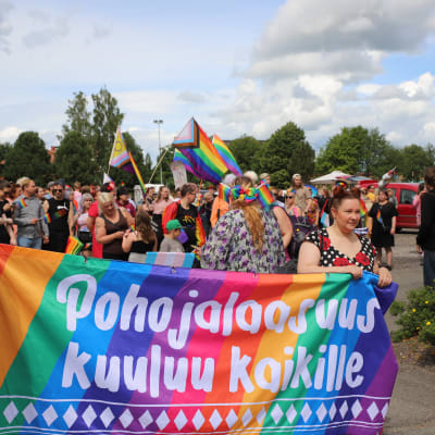 Pride-tapahtumassa liikkuvia ihmisiä Lapualla aurinkoisena kesäisenä päivänä, kuvissa näkyy sateenkaarilippuja.