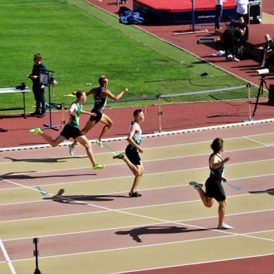 Johan Grönroos passerar mållinjen efter ett 100 meters lopp på Paavo Nurmi stadion. På bilden syns flera andra löpare också.