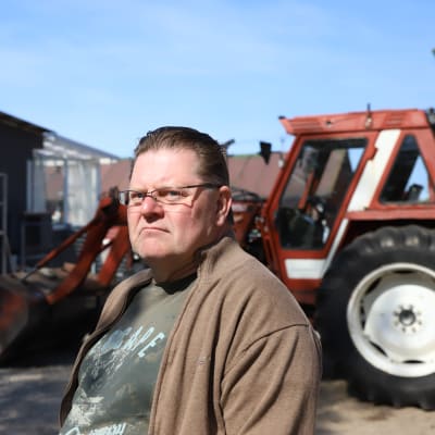 Maaseudulla asuva Pekka Tiikkala seisoo kotipihallaan traktorinsa edessä.