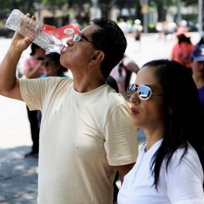 En man dricker vatten ur en flaska, bredvid honom människor.