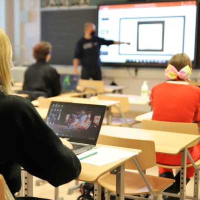 Abiturienter sitter i ett klassrum och lyssnar på en lärare som pekar på något.